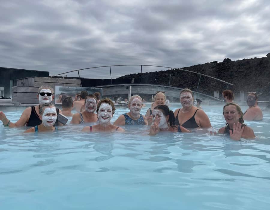 A group of midlife women in a lagoon in Iceland; some have clay masks on their face.