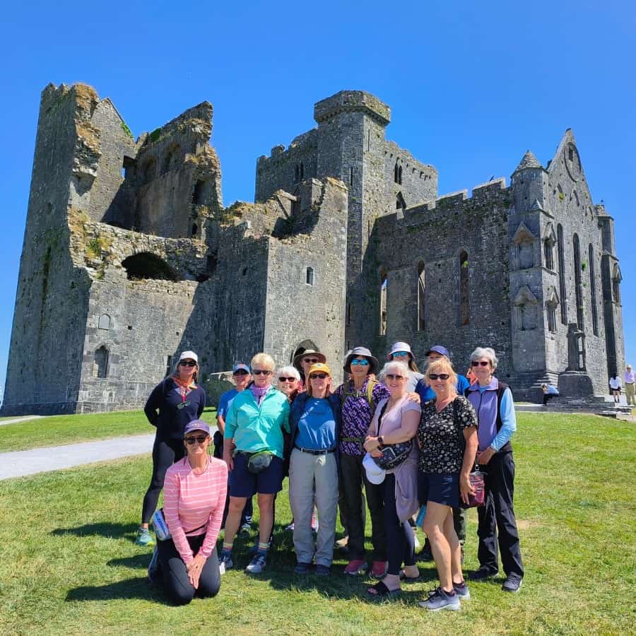 A group of middle-aged women travelers pose on front of a castle on a hiking trip in Ireland.