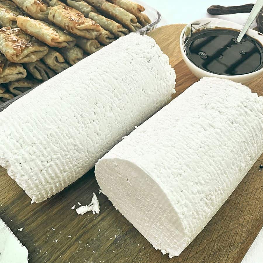 Two long rounds of Cyprus Anari cheese sit on a platter with a bowl of dark sauce accompanying it.