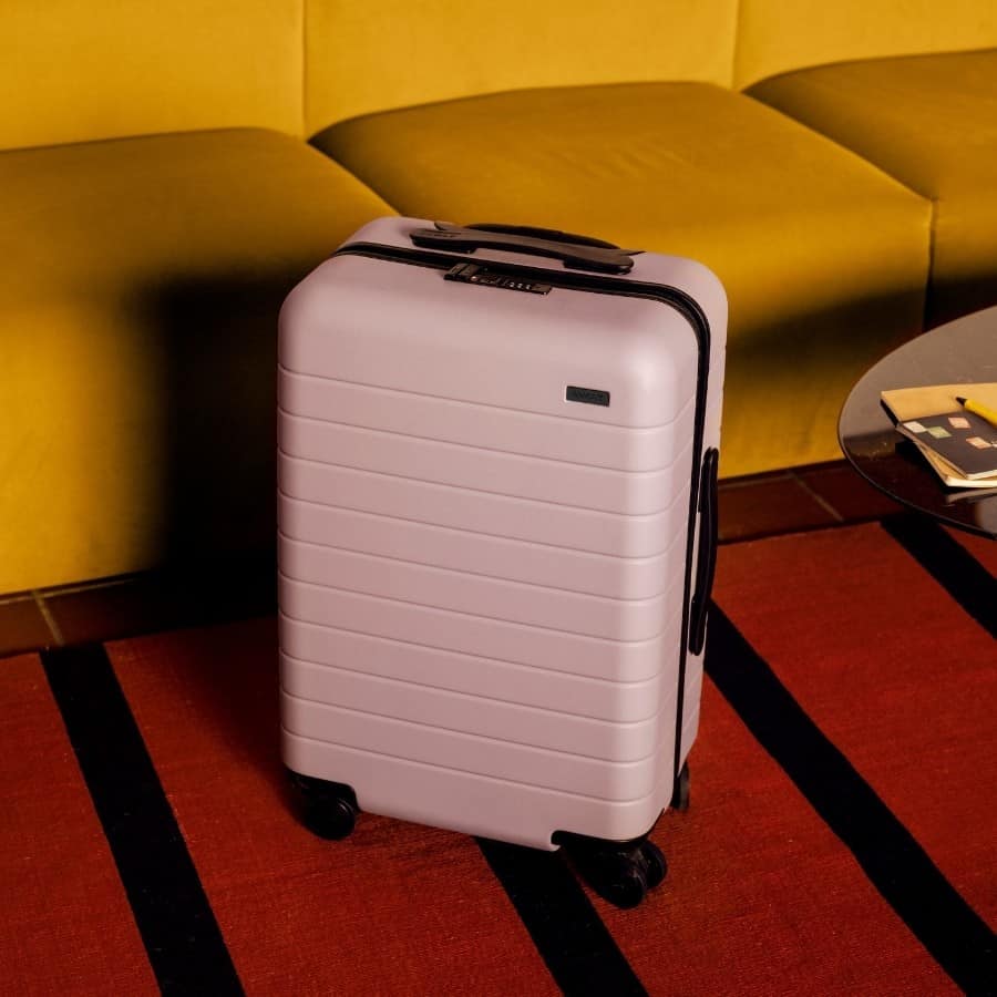 Away Carry on Bag in Blush set in a colorful living room with a striped rug