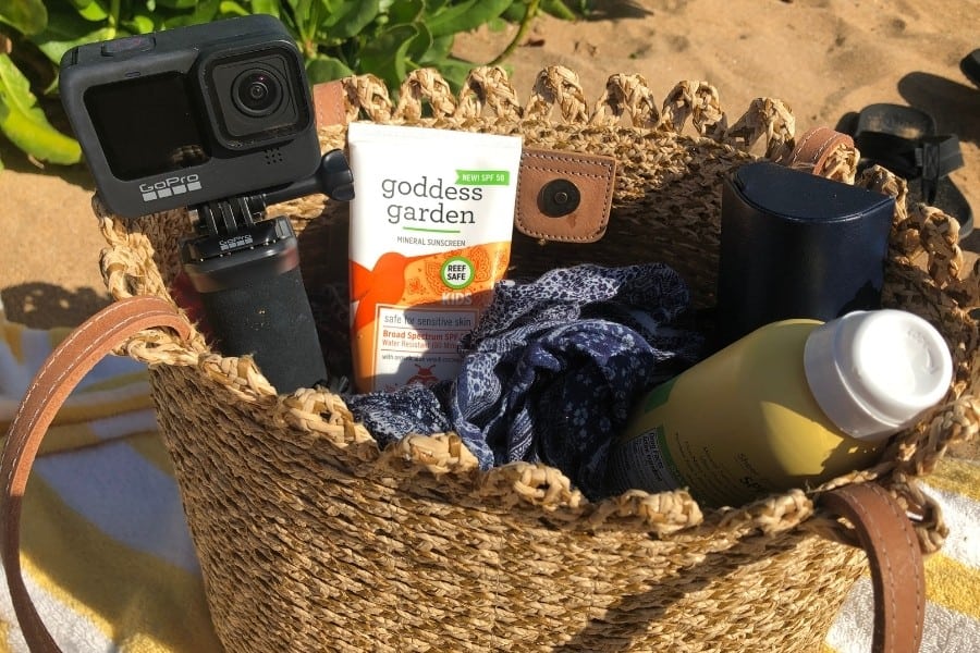 A woven beach bag with a GoPro camera, sunscreen and cover up visible