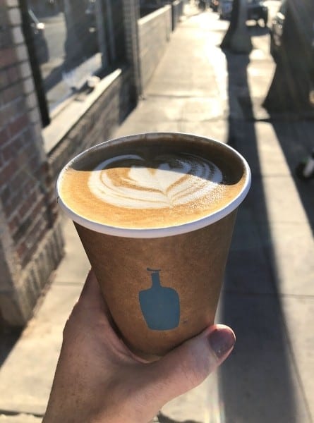 A hand holds a cup of blue bottle coffee in Venice California