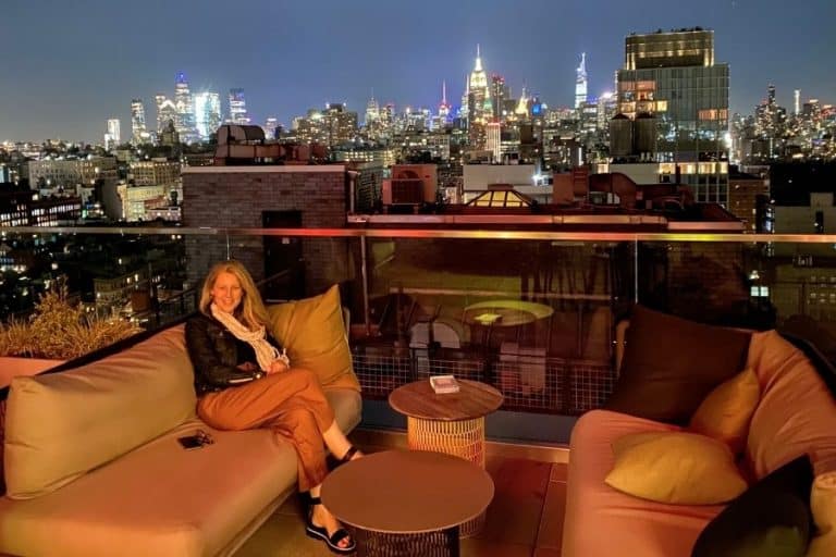 Susan Heinrich sits on a rooftop lounge in New York City withe the city and buildings beyond