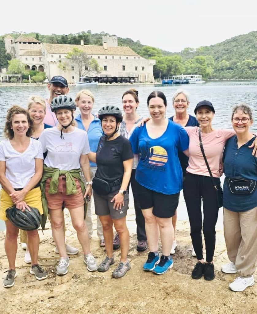 A group of ten midlife and older adult women stand in front of a lake in Croatia. One man is also partially visible at the back.