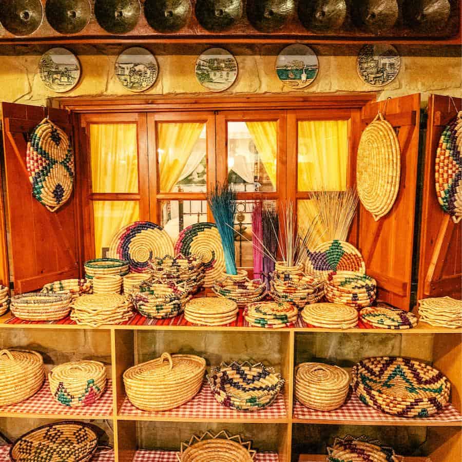 Colorful baskets in a traditional Cypriot style hang on a wall and are stacked on shelves in a traditional space with wood and red accents.