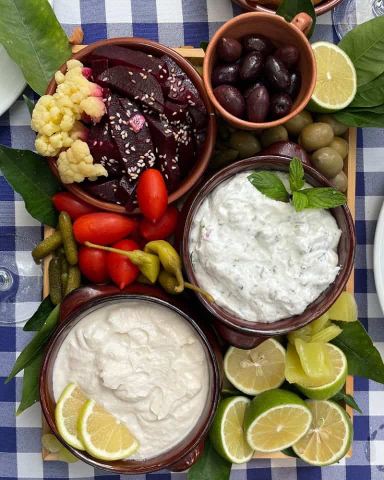 A Cyprus meze platter: olives, beets, limes, tzatziki, tomatoes and limes sit atop a checked table cloth