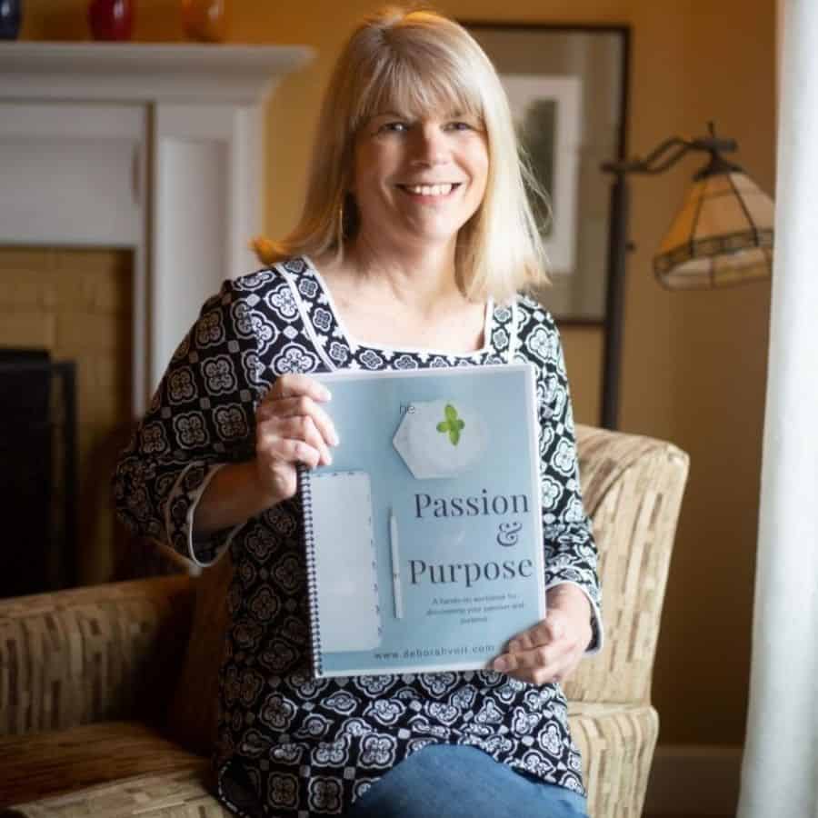 Deborah Voll, offers coaching for women. She's pictured sitting on a chair, holding her workbooks..