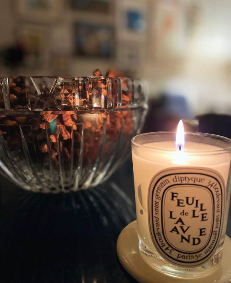 A French diptyque candle is lit in the foreground with a crystal bowl filled with pinecones just behind it.