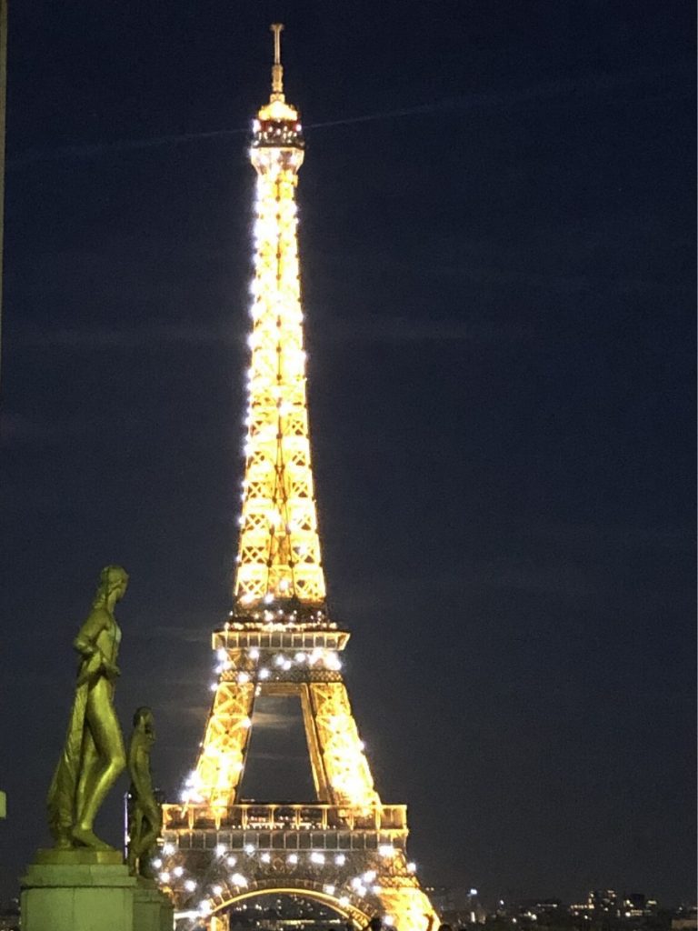 Eiffel tower illuminated at night, visible from the Trocadero Paris. A statue of a goddess is visible in the foreground.
