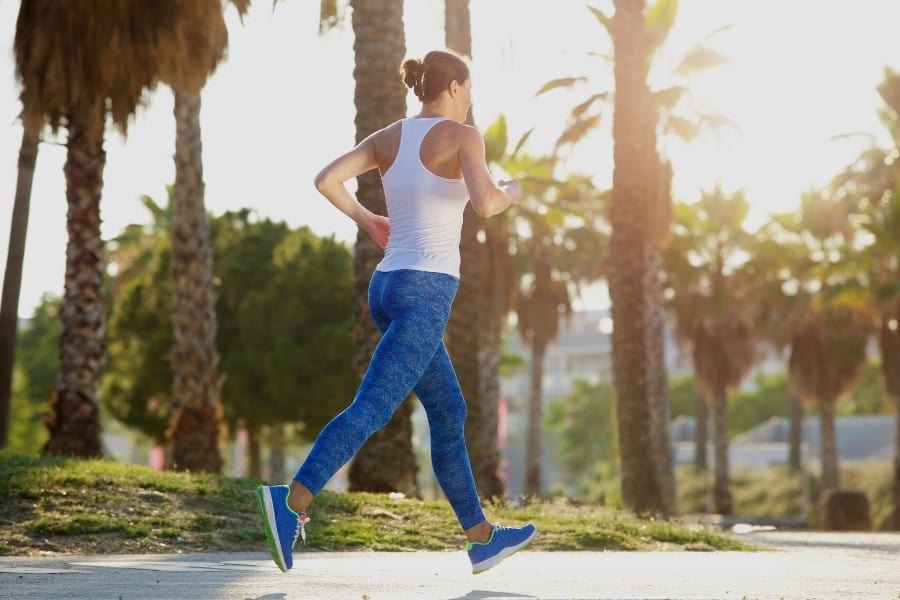 A midlife woman runs on a path lined with palm trees
