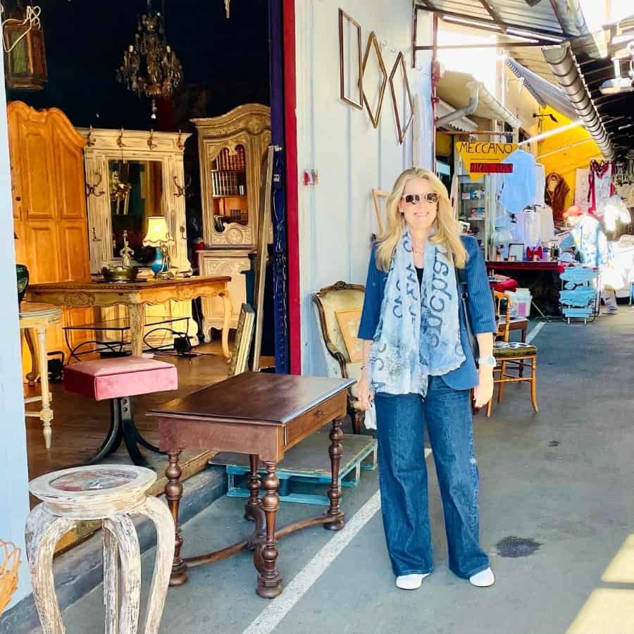 Susan Heinrich wears blue jeans and a blue blazer and scarf at the Puces antique market in Paris.