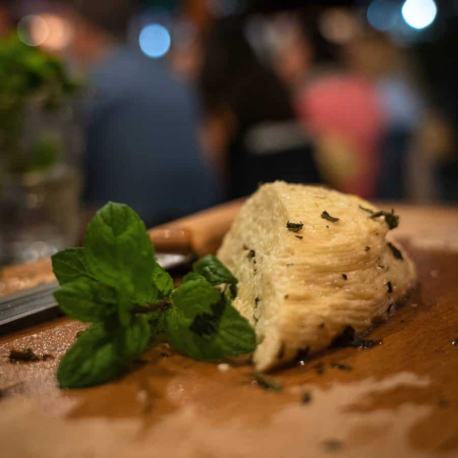 A piece of fresh Cyprus halloumi sits on a wooden board sprinkled with fresh herbs and a garnish of mint