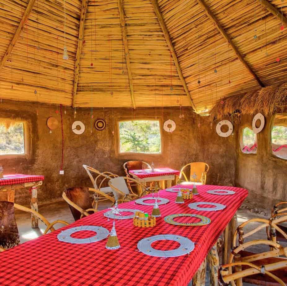 A traditional Maasai tent with a woven roof, has a table set with dishes and a bright red cloth, ready to welcome tourists for a meal, near Moshi Tanzania.