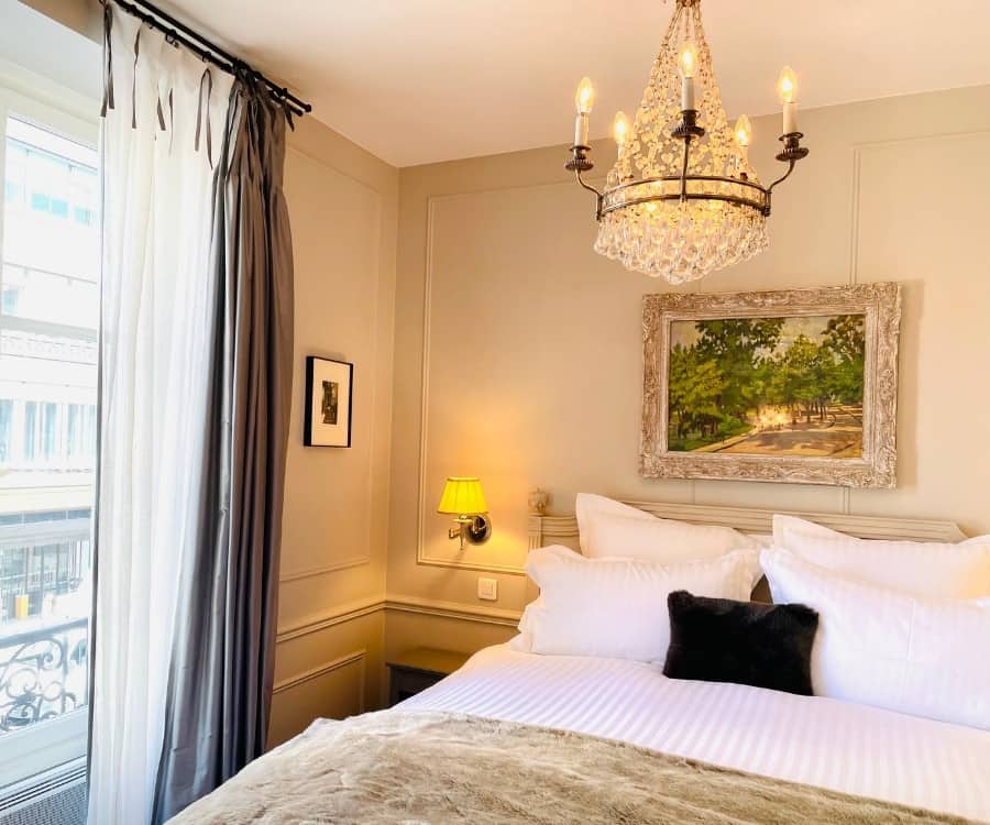 A bed with a beautiful chandelier and French window in a holiday apartment in Paris w