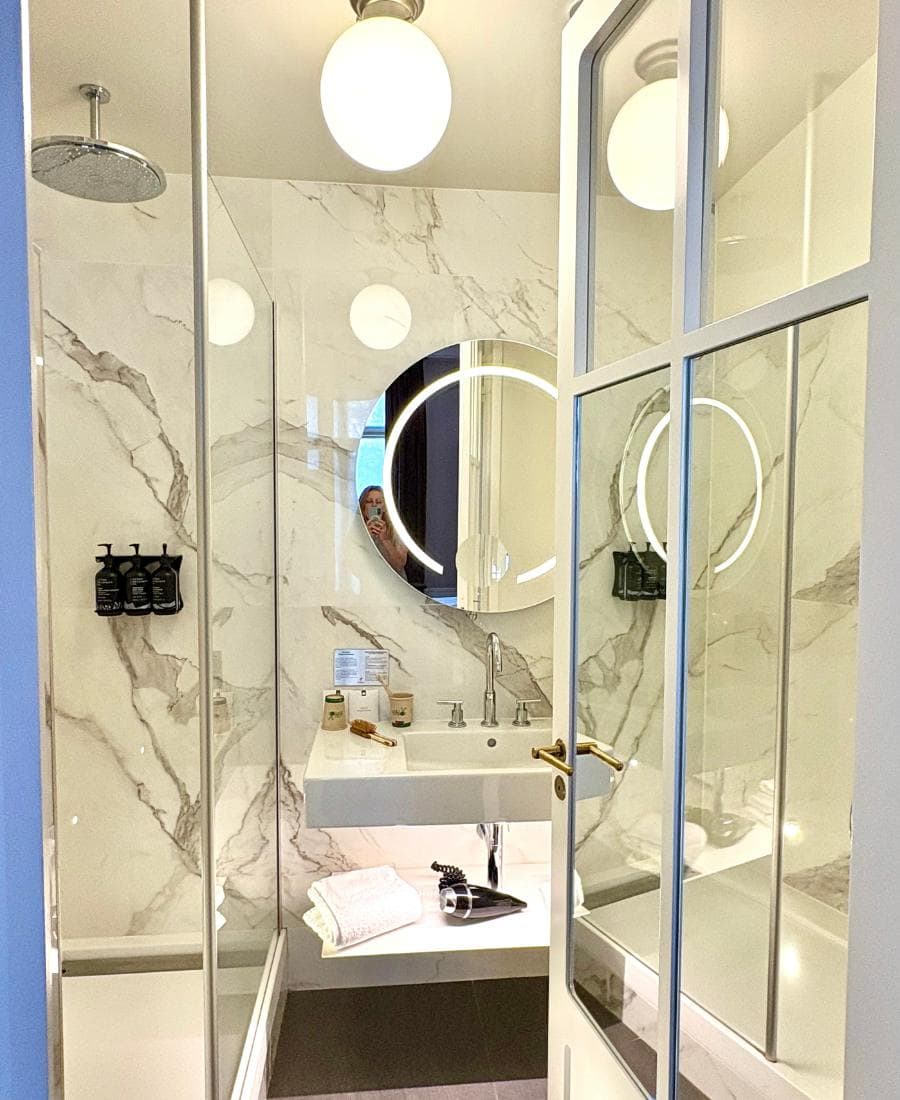 A modern hotel bathroom with white marble, a small vanity and lots of glass.