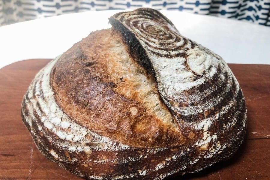 A loaf of homemade sourdough bread looks inviting, on a wood cutting board