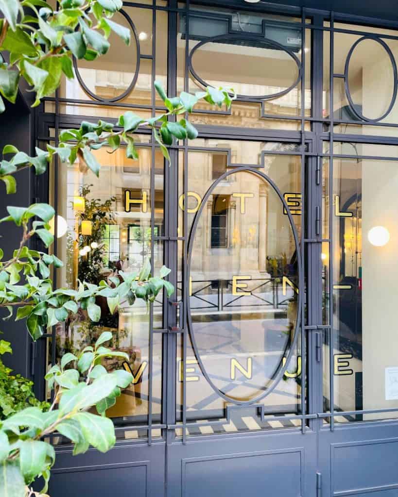 An ornate blue door at a hotel entrance edged on one side by greenery.