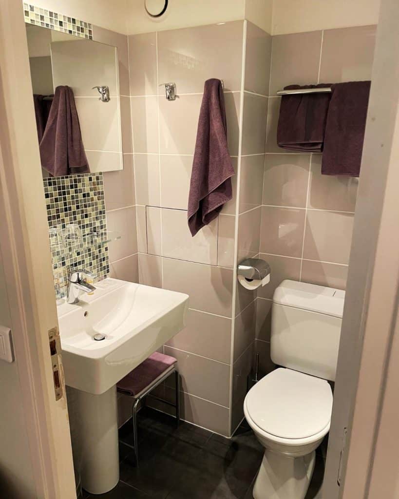 A small but modern bathroom with a small square tile behind the sink and grey tile floor.