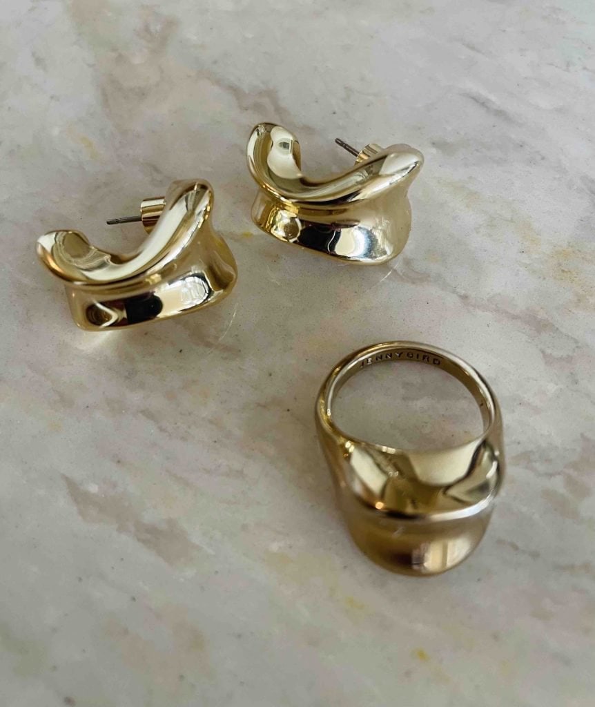 Chunky gold earrings and a ring are pictured on a marble surface.
