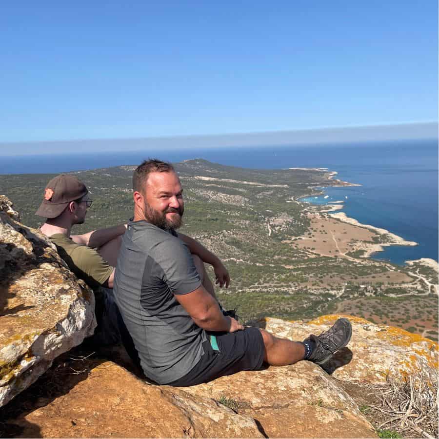 A man sits on top of a rock with a view of a coastline and the Mediterranean beyond