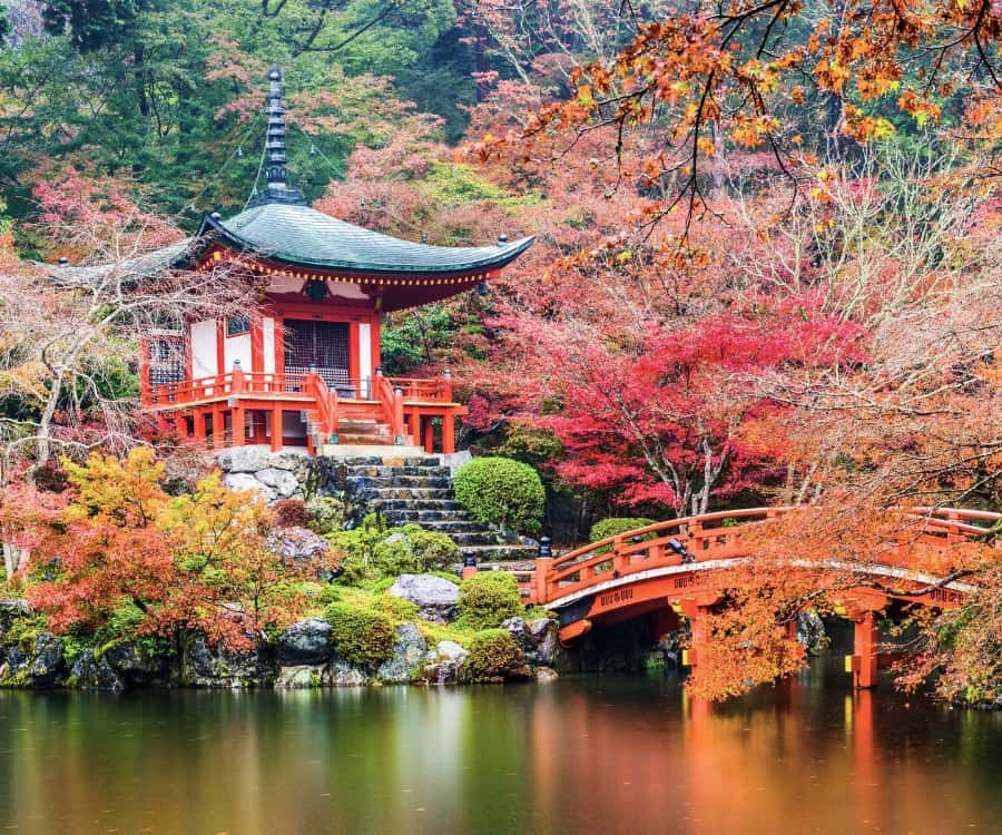 Daigoji Temple in Fushimi-ku, Kyoto Japan with fall leaves in the background. A small temple and bridge are in the foreground.