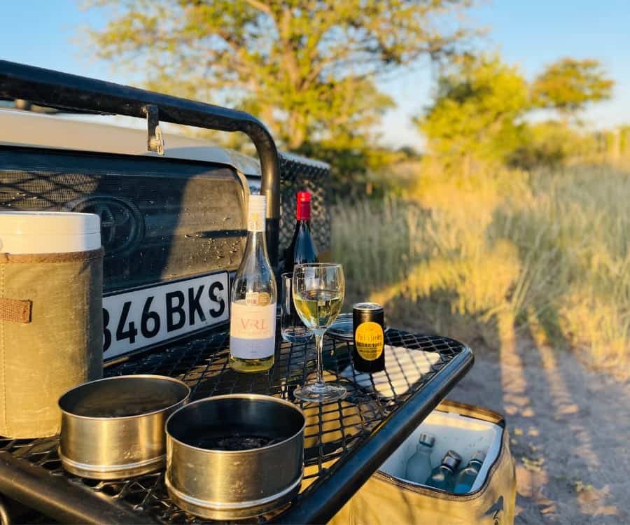Sundowner time in the Magkadikgadi Pans National Park. A jeep is parked with bottles and snacks set out on tray that extends from its front.