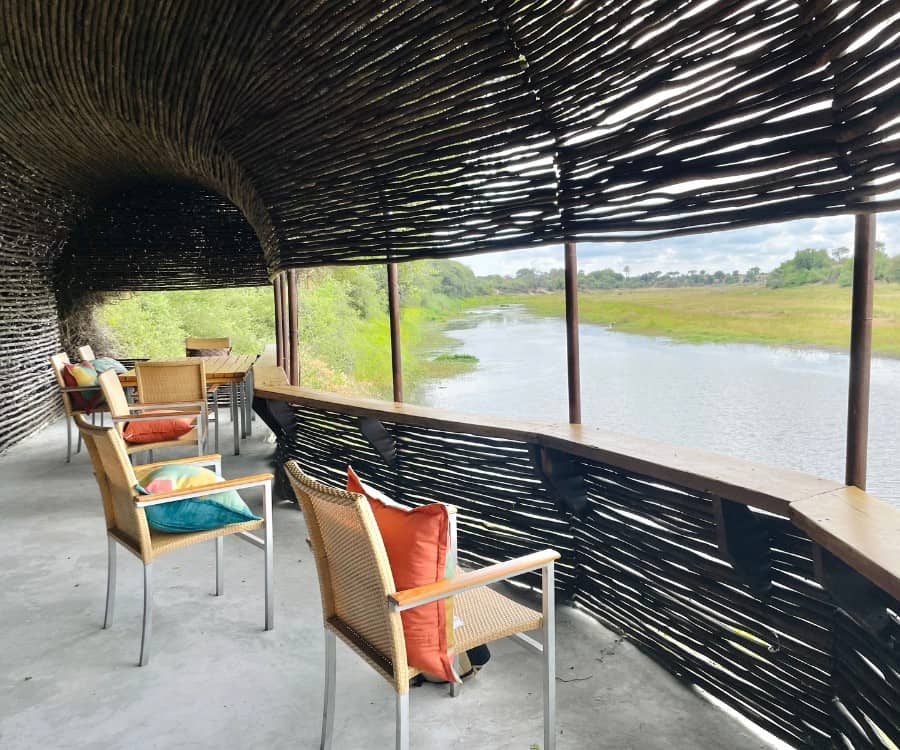 The wildlife viewing hide at Leroo La Tau safari camp in Botswana. Pictured are several chairs with colorful pillows and the Boteti River outside the hide.