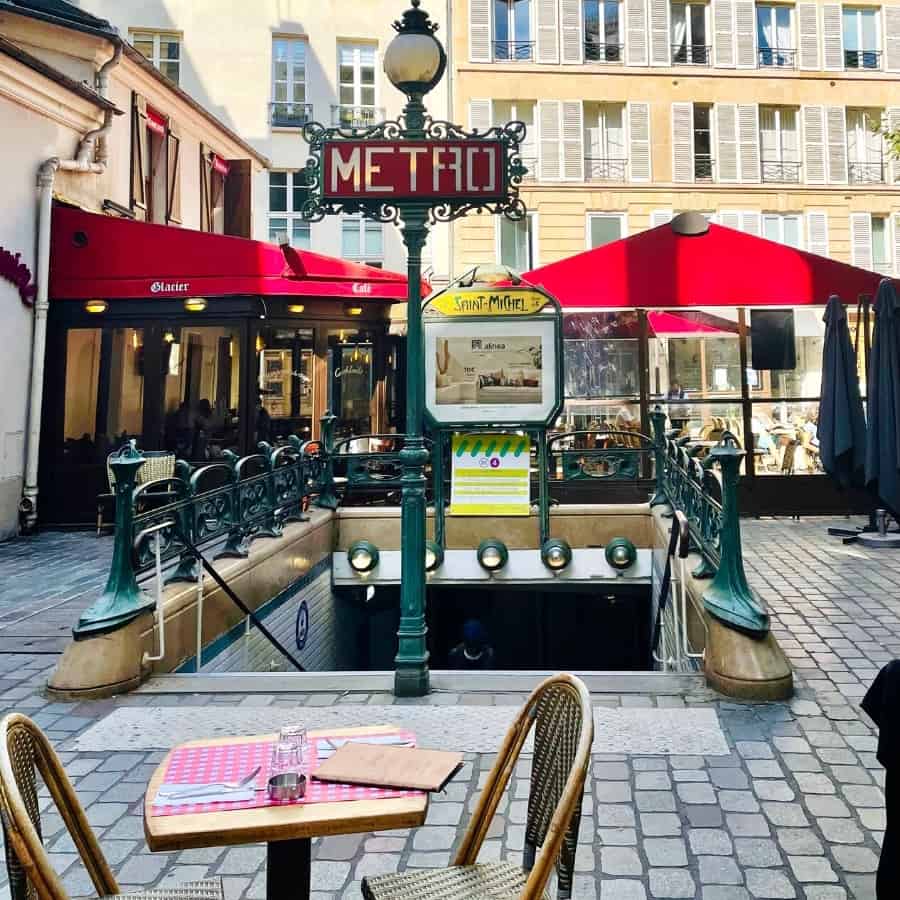 A bistro table with two chairs in front of the entrance to a Metro station in Paris