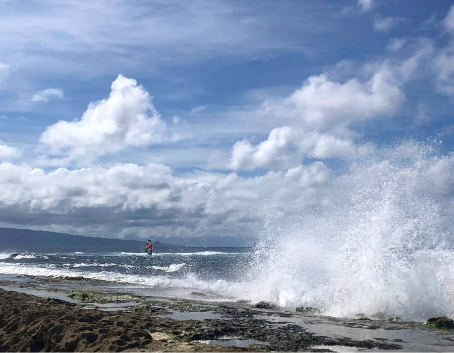 Waves crash on the shore and a windsurfer is in the distance at Ho‘okipa Beach in Maui