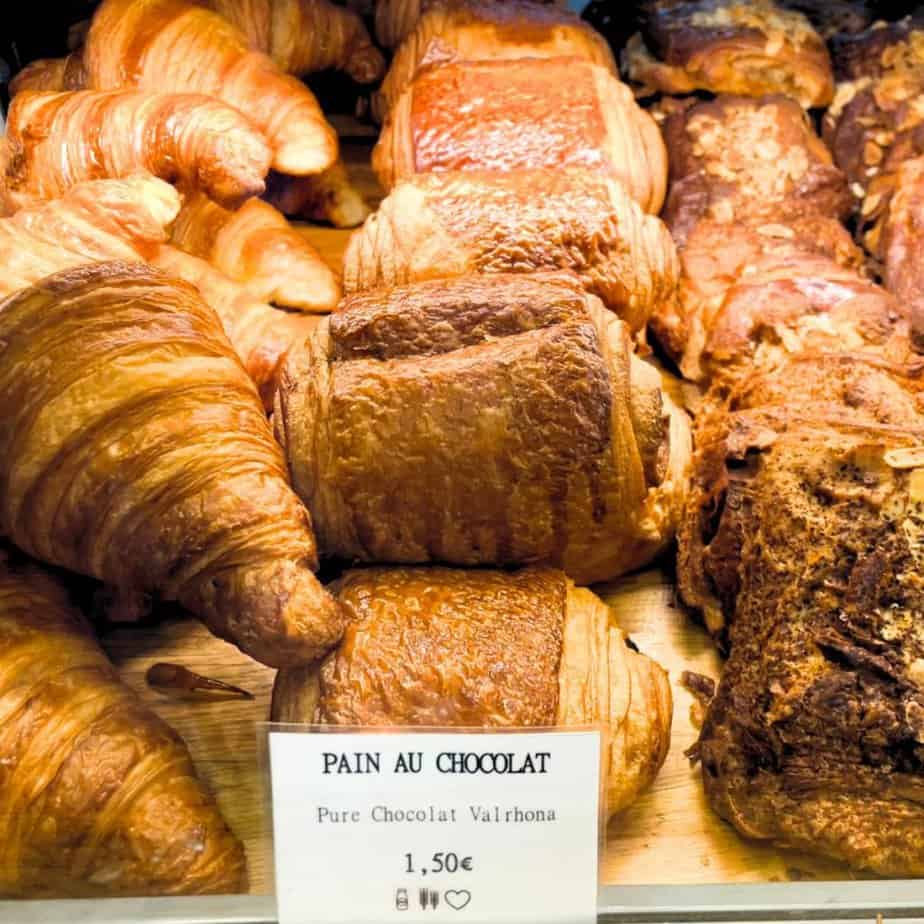 A row of Paris pain au chocolat croissants sit together in a glass case next to butter croissants.