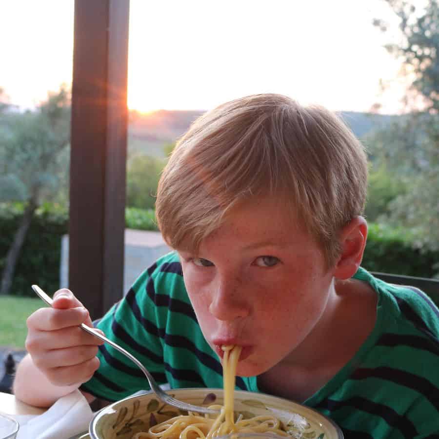 A young boy eats pasta with a view of the Umbrian hills beyond him