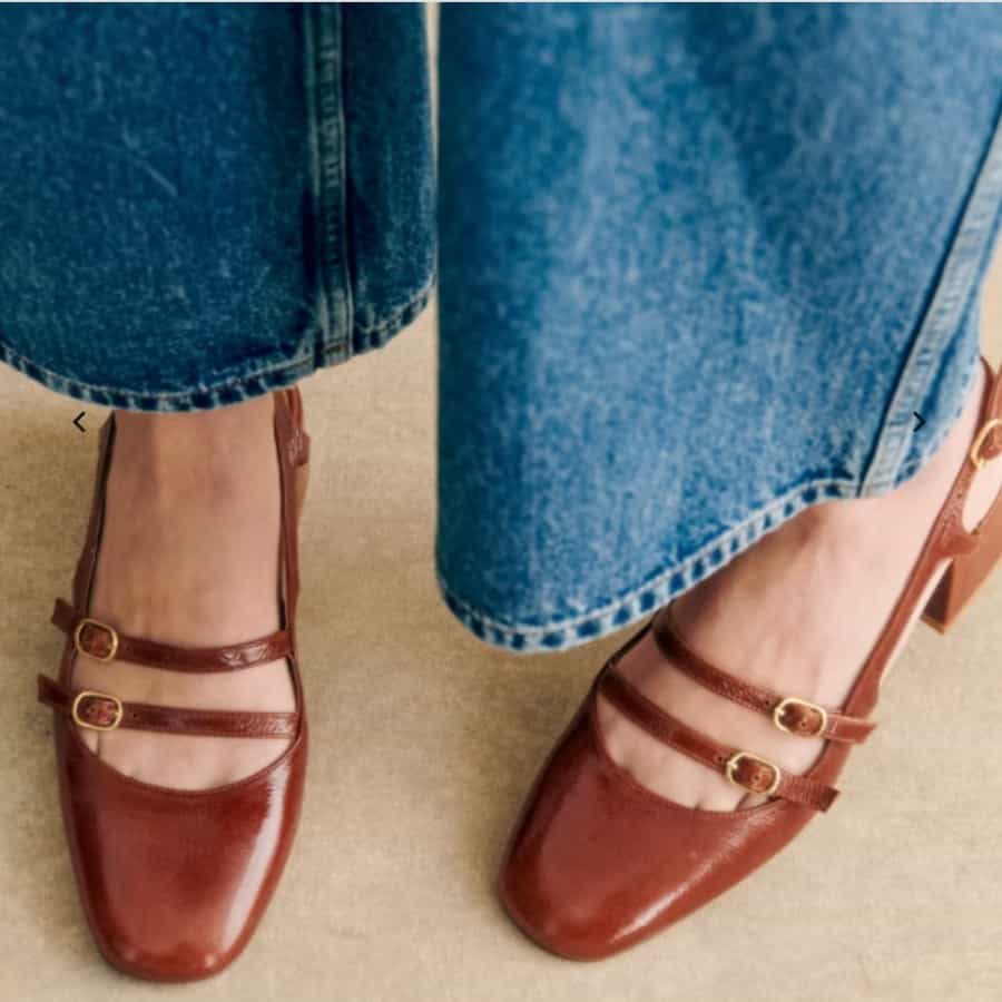 A pair of camel-colored Mary Jane style shoes being worn with a little of the person's wide-leg denim jeans visible.