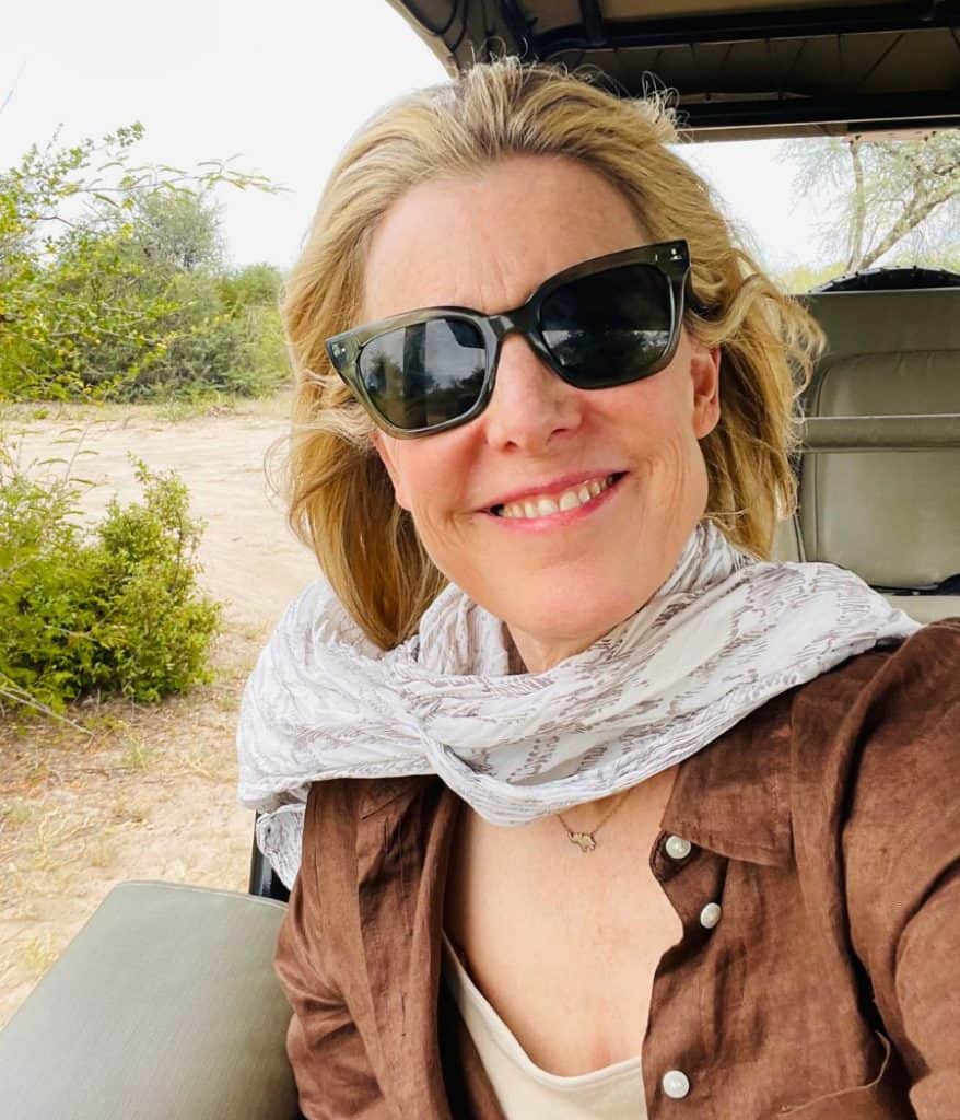 Susan Heinrich rides in a safari jeep with green Warby Parker sunglasses on.
