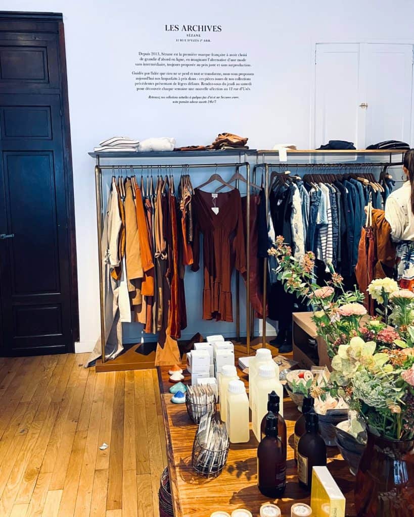A selection of sales clothing and accessories is visible at the Sézane archives store. Many hanging items are white, beige and brown.
