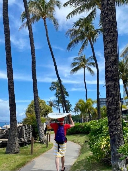 A man wlaks with a surfboard on his head at Kaanapali Beach Maui