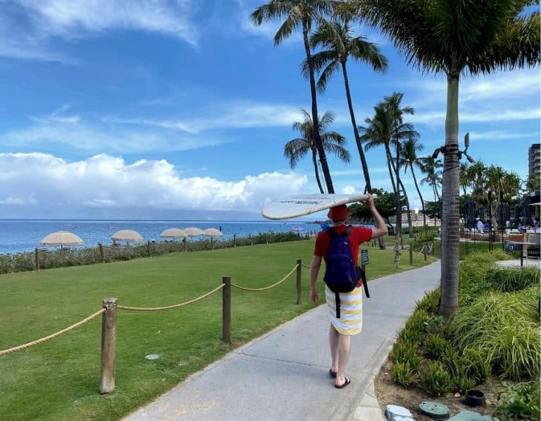 A man carries a surfboard on his head as he walks next to Kaanapali Beach Maui