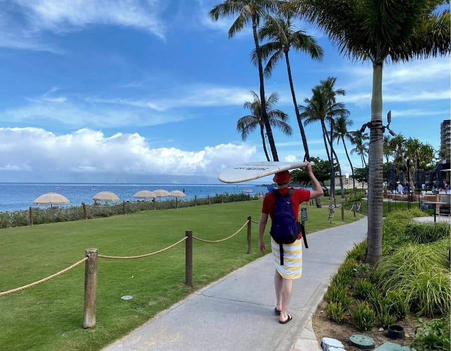 A man carries a surfboard on his head as he walks next to Kaanapali Beach Maui
