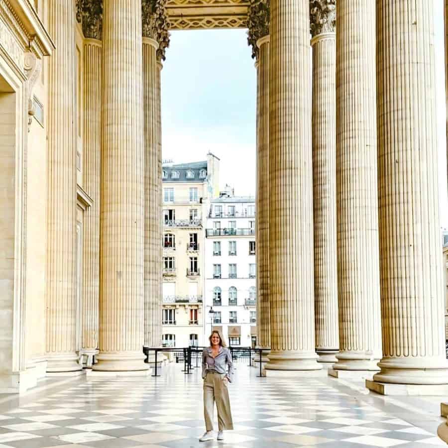 Susan Heinrich stands at the entrance to the Pantheon Paris, a historic monument in Paris's Latin Quarter. Pictured are enormous pillars, a marble entry floor and buildings beyond.