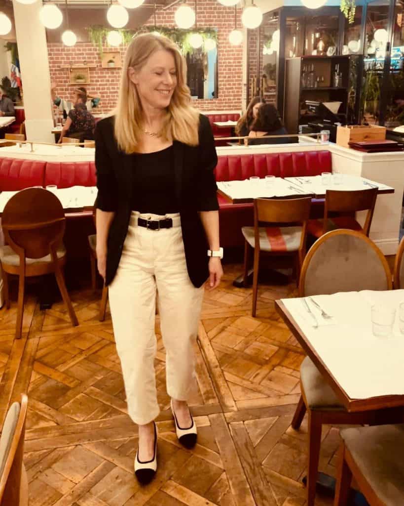 Susan Heinrich wears classic French style at a Paris bistro: a black blazer with cream trousers and cream shoes with a black toe cap.
