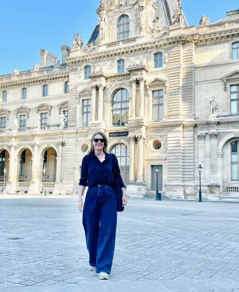 A woman stands in a courtyard in front of a French building made of white limestone.