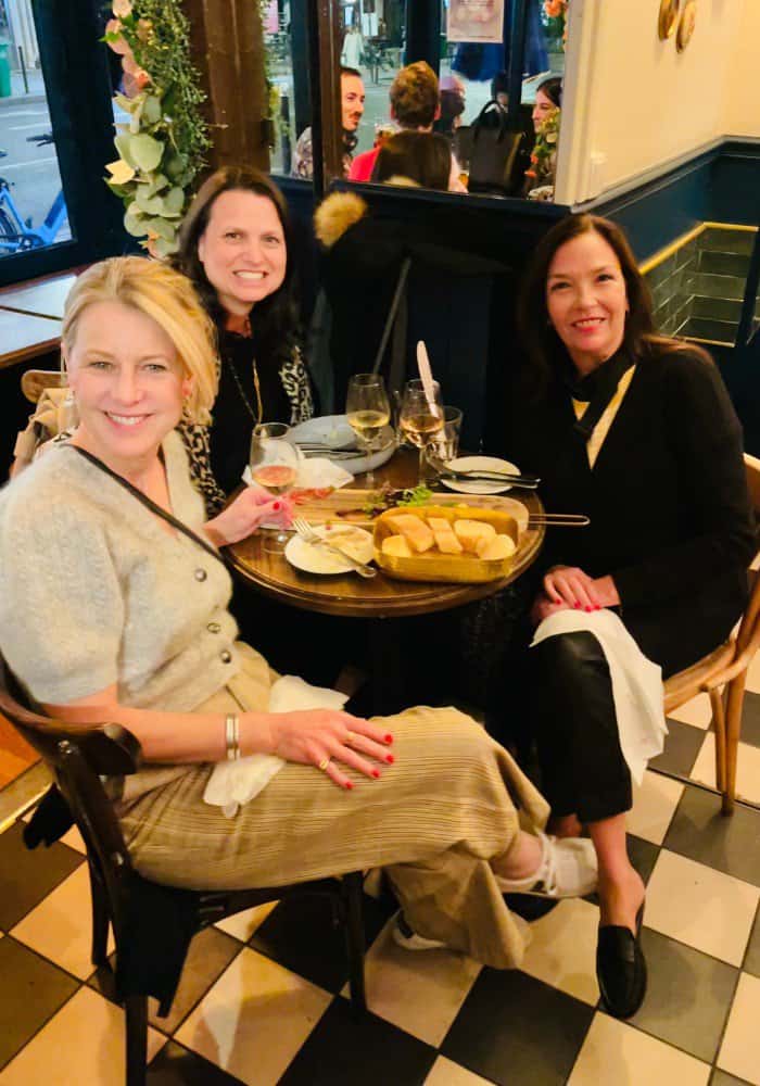 Susan Heinrich and two women friends sit at a table in a bistro in Paris. There is bread and some other food in the table.