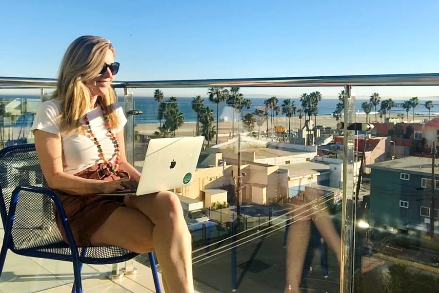 Susan Heinrich sits typing on a laptop and overlooking the Pacific Coast in L.A.