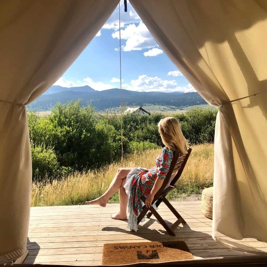 A woman sits on a wooden tent platform looking at the view at Under Canvas Yellowstone