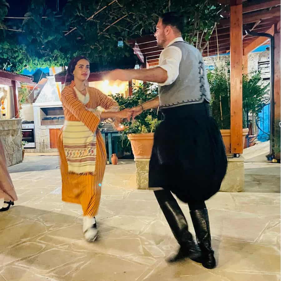 A man and a woman were traditional Cypriot costumes and hold hands as they are dancing in an open-air courtyard.
