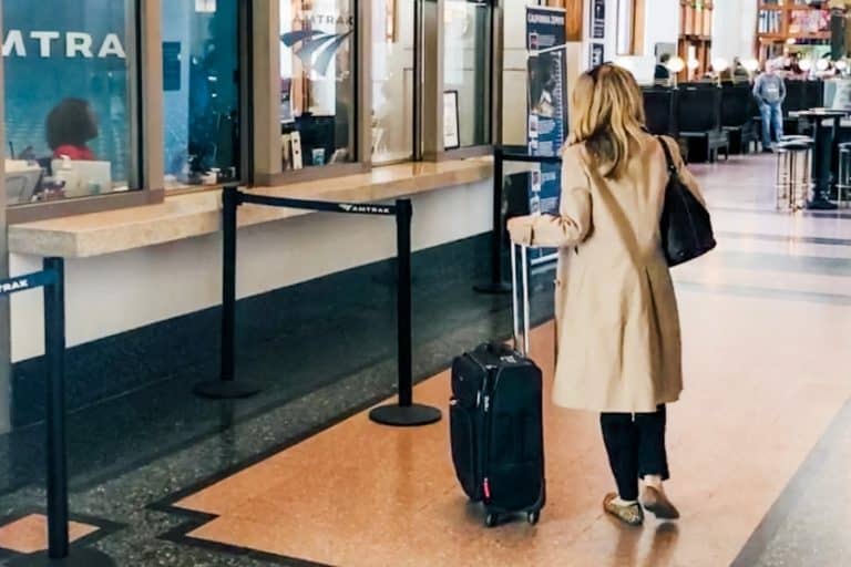 A woman walks through a train station with carry-on luggage