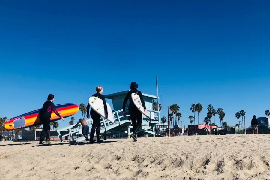 Three women surfers carry their boards on Venice Beach California