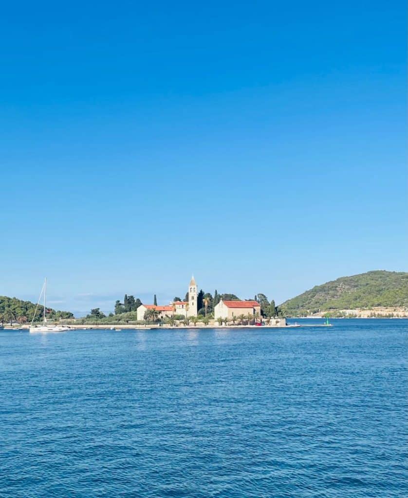 A small island with old red-roofed buildings sits in the turquoise Adriatic Sea.