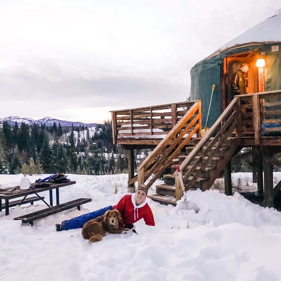 A young man and dog lay in the snow outside a yurt at Pearl Lake State Park